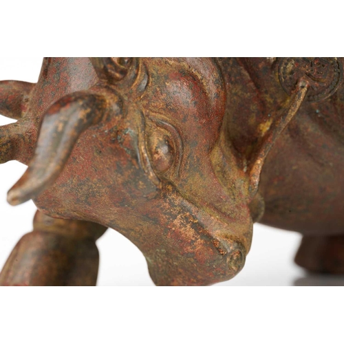 198 - A Chinese bronze figure of a charging bull, wearing a band of good luck charms, traces of red pigmen... 