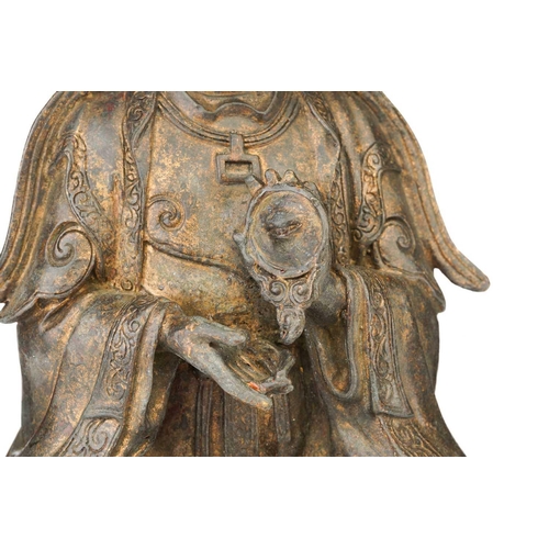 92 - A Chinese bronze figure of Guanyin, seated wearing long robes and holding a mirror, traces of red pi... 