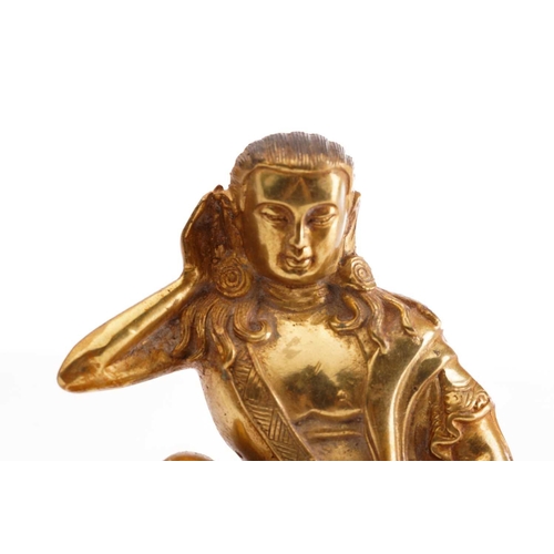 180 - A Chinese gilt bronze figure of Milarepa, seated with his right hand cupped to his ear, a bowl in hi... 