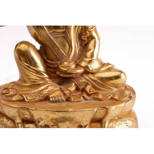 180 - A Chinese gilt bronze figure of Milarepa, seated with his right hand cupped to his ear, a bowl in hi... 