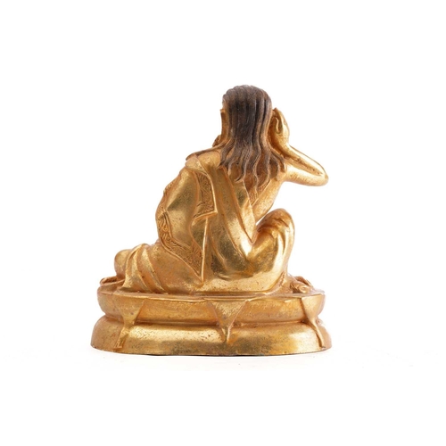 180 - A Chinese gilt bronze figure of Milarepa, seated with his right hand cupped to his ear, a bowl in hi... 