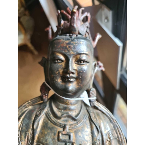 182 - A Chinese bronze figure of Guanyin, seated wearing long robes and holding a mirror, traces of red pi... 