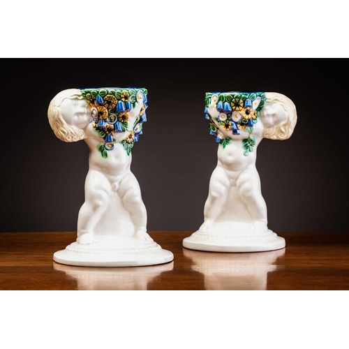 79 - Michael Powolny (1871-1954) Austrian, a pair of ceramic candlesticks, modelled as putti supporting a... 