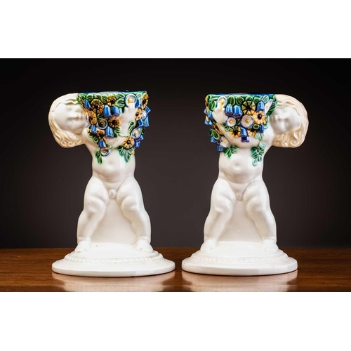 79 - Michael Powolny (1871-1954) Austrian, a pair of ceramic candlesticks, modelled as putti supporting a... 