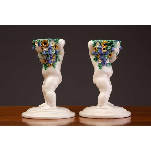 79 - Michael Powolny (1871-1954) Austrian, a pair of ceramic candlesticks, modelled as putti supporting a... 