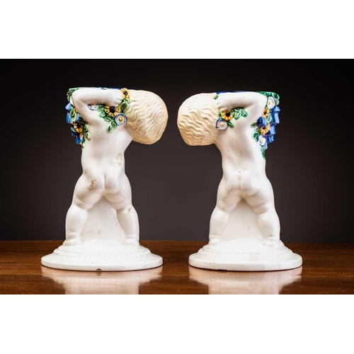 79 - Michael Powolny (1871-1954) Austrian, a pair of ceramic candlesticks, modelled as putti supporting a... 