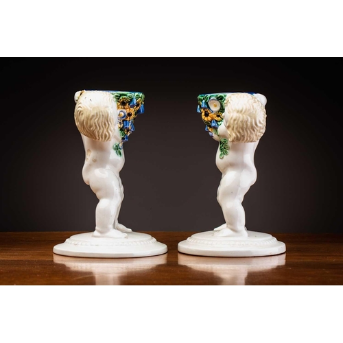 79 - Michael Powolny (1871-1954) Austrian, a pair of ceramic candlesticks, modelled as putti supporting a... 