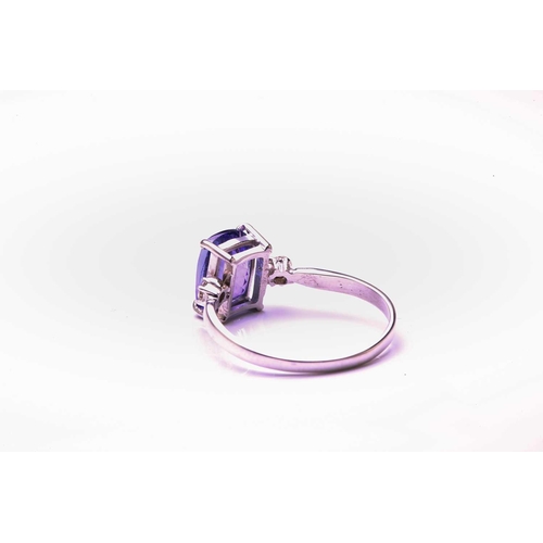 130 - A single stone tanzanite ring with diamond set shoulders; the oval cut tanzanite in four claw mount ... 