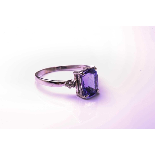 130 - A single stone tanzanite ring with diamond set shoulders; the oval cut tanzanite in four claw mount ... 