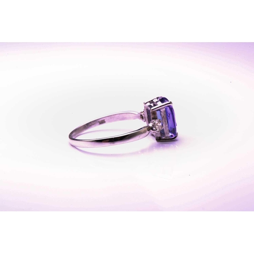 130 - A single stone tanzanite ring with diamond set shoulders; the oval cut tanzanite in four claw mount ... 