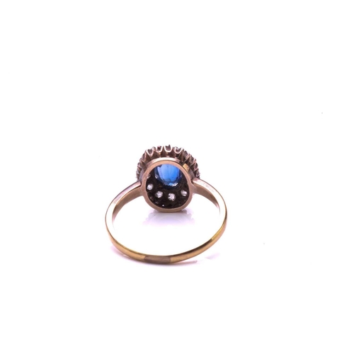 183 - A sapphire and diamond cluster ring; the oval cut sapphire claw mounted within a border of mixed old... 