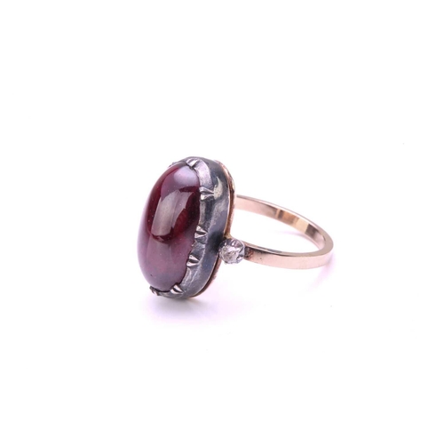 232 - A foil-backed garnet and diamond dress ring, contains a long oval garnet cabochon in scalloped colle... 