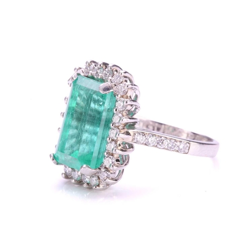 299 - An emerald and diamond halo ring in platinum, featuring a rectangular emerald-cut emerald with brigh... 