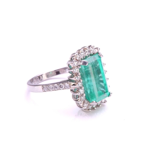 299 - An emerald and diamond halo ring in platinum, featuring a rectangular emerald-cut emerald with brigh... 