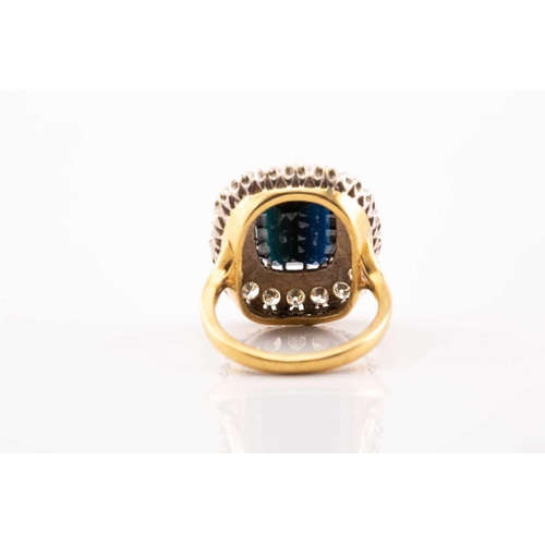 40 - A sapphire and diamond cluster ring in 18ct gold, featuring an emerald-cut sapphire with a dark blue... 