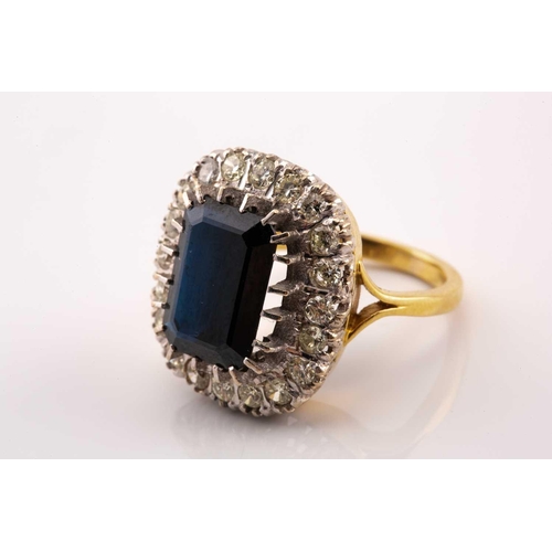 40 - A sapphire and diamond cluster ring in 18ct gold, featuring an emerald-cut sapphire with a dark blue... 