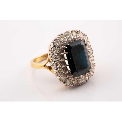 40 - A sapphire and diamond cluster ring in 18ct gold, featuring an emerald-cut sapphire with a dark blue... 