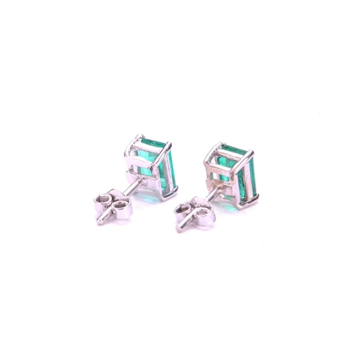 54 - A pair of emerald stud earrings, each comprising a rectangular emerald-cut emerald with intense gree... 