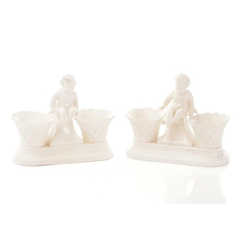 440 - A pair of Berlin salts, each with a putto standing over two bowls and scrolling feet painted with bi... 