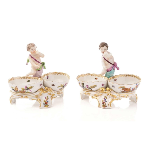 440 - A pair of Berlin salts, each with a putto standing over two bowls and scrolling feet painted with bi... 