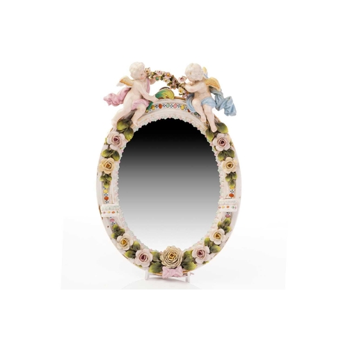 449 - A Dresden style floral encrusted wall mirror, the oval plate surmounted by cherubs with a garland of... 