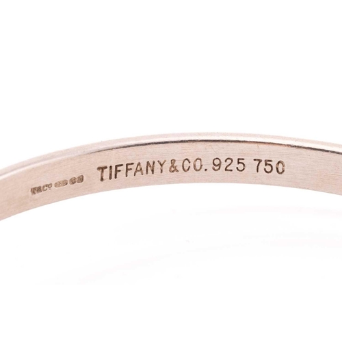 130 - Tiffany & Co. - A two-tone hook and eye bangle, comprising an oval-shaped flat bangle bracelet, sign... 