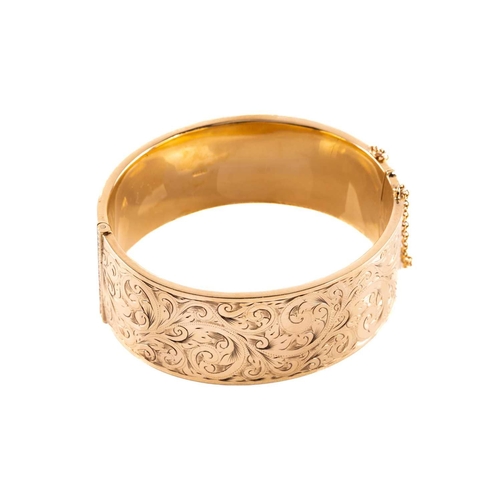 17 - A 9ct yellow gold hinged bangle, the hollow bracelet is engraved with scrollwork design, completed w... 