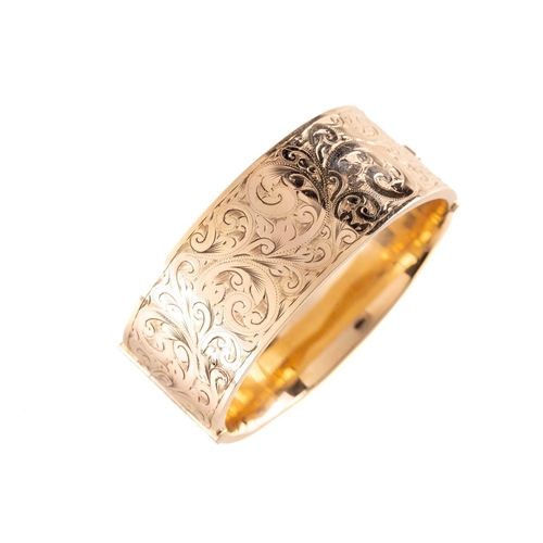 17 - A 9ct yellow gold hinged bangle, the hollow bracelet is engraved with scrollwork design, completed w... 