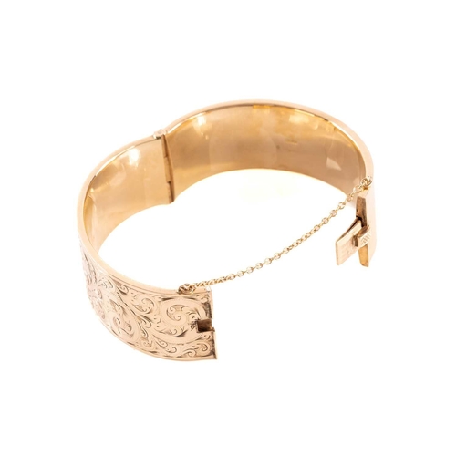 17 - A 9ct yellow gold hinged bangle, the hollow bracelet is engraved with scrollwork design, completed w... 