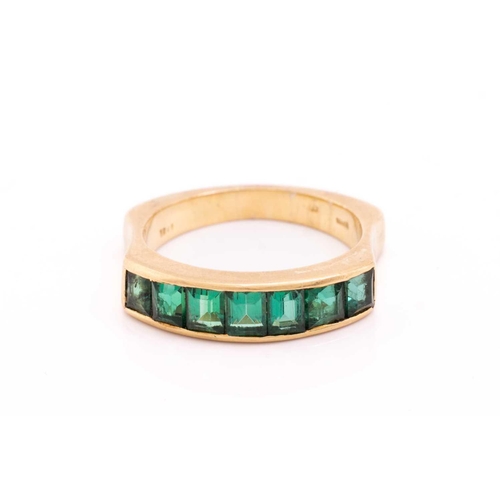 194 - An emerald half-eternity ring, channel-set with a row of seven step-cut emeralds, to an ergonomic ri... 