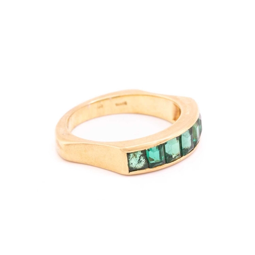 194 - An emerald half-eternity ring, channel-set with a row of seven step-cut emeralds, to an ergonomic ri... 