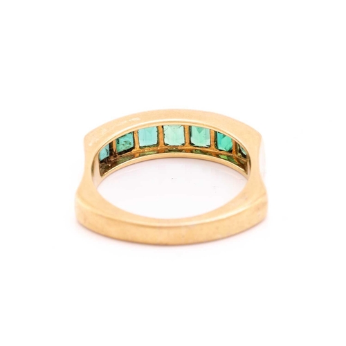 194 - An emerald half-eternity ring, channel-set with a row of seven step-cut emeralds, to an ergonomic ri... 