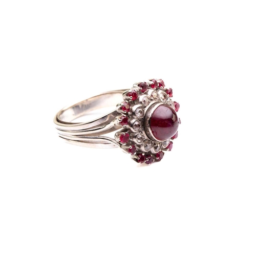 208 - A cabochon ruby and diamond cluster ring; the central, circular ruby in collet mount above a border ... 