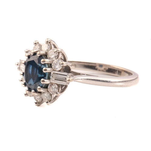 211 - A sapphire and diamond cluster ring in 18ct white gold, consisting of an oval-cut sapphire with deep... 