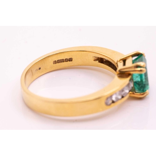 216 - An emerald and diamond dress ring in 18ct yellow gold, centred with an emerald-cut emerald with brig... 