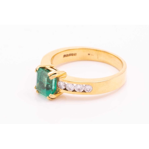 216 - An emerald and diamond dress ring in 18ct yellow gold, centred with an emerald-cut emerald with brig... 