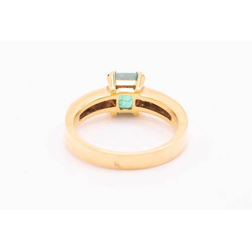 216 - An emerald and diamond dress ring in 18ct yellow gold, centred with an emerald-cut emerald with brig... 