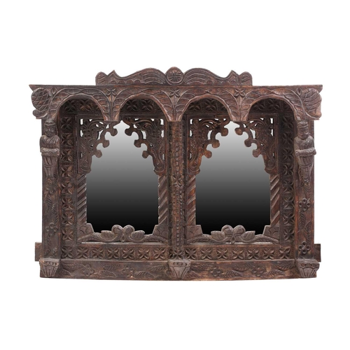 128 - An Indian rustic carved teakwood over mantle mirror with overhanging arcaded cornice above a pair of... 