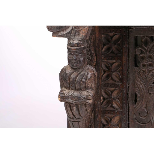 128 - An Indian rustic carved teakwood over mantle mirror with overhanging arcaded cornice above a pair of... 