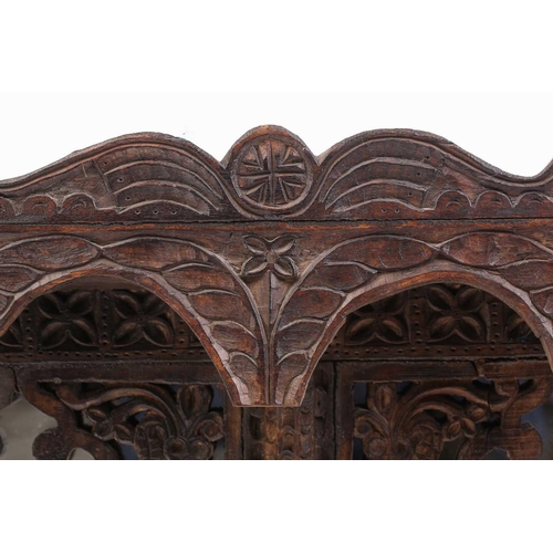 128 - An Indian rustic carved teakwood over mantle mirror with overhanging arcaded cornice above a pair of... 