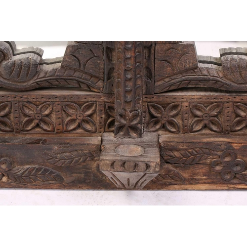 128 - An Indian rustic carved teakwood over mantle mirror with overhanging arcaded cornice above a pair of... 