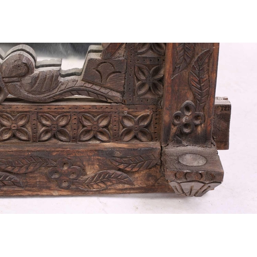 128 - An Indian rustic carved teakwood over mantle mirror with overhanging arcaded cornice above a pair of... 