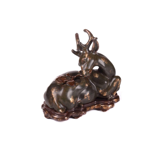 127 - A Chinese porcelain simulated bronze figure of a recumbent stag with a sprig of lingzhi, the green g... 