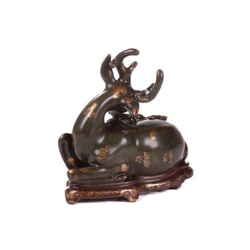 127 - A Chinese porcelain simulated bronze figure of a recumbent stag with a sprig of lingzhi, the green g... 