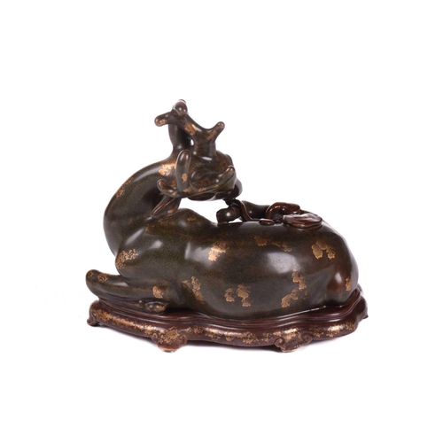 127 - A Chinese porcelain simulated bronze figure of a recumbent stag with a sprig of lingzhi, the green g... 