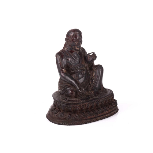 153 - A Chinese bronze figure of a Tibetan Buddhist master, seated in robes and holding a small conch shel... 