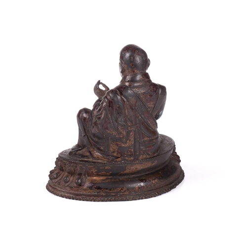 153 - A Chinese bronze figure of a Tibetan Buddhist master, seated in robes and holding a small conch shel... 