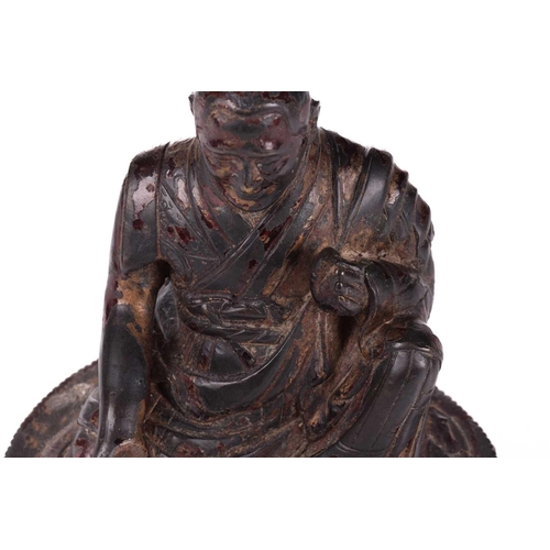 153 - A Chinese bronze figure of a Tibetan Buddhist master, seated in robes and holding a small conch shel... 