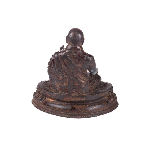 153 - A Chinese bronze figure of a Tibetan Buddhist master, seated in robes and holding a small conch shel... 