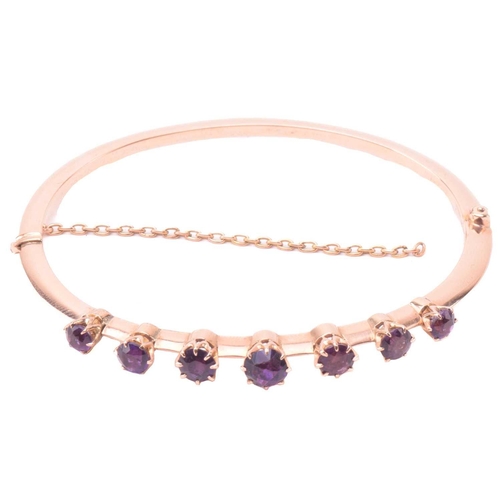 137 - A late Victorian amethyst hinged bangle, set with a row of four amethysts and three purple paste, to... 